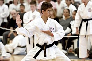 a teenage boy wearing a black belt performs a karate move in front of spectators