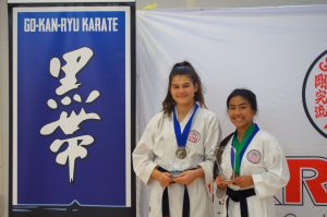 two young students standing next to the gkr karate black belt open tournament banner