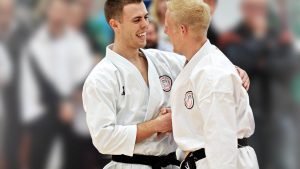 two young men wearing karate gi handshake and give each other pat on the back in front of crowd