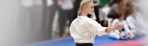 a blonde teenager wearing a black belt performs a karate move