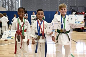 three kids standing proud with medals and certificates