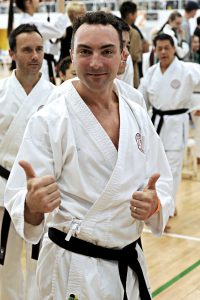 a man wearing a gi who poses for the camera with two thumbs up
