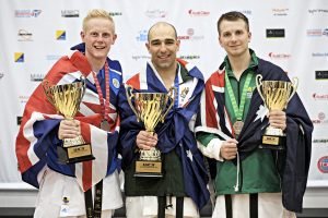 three men wearing there country flags as capes, they are holding trophies