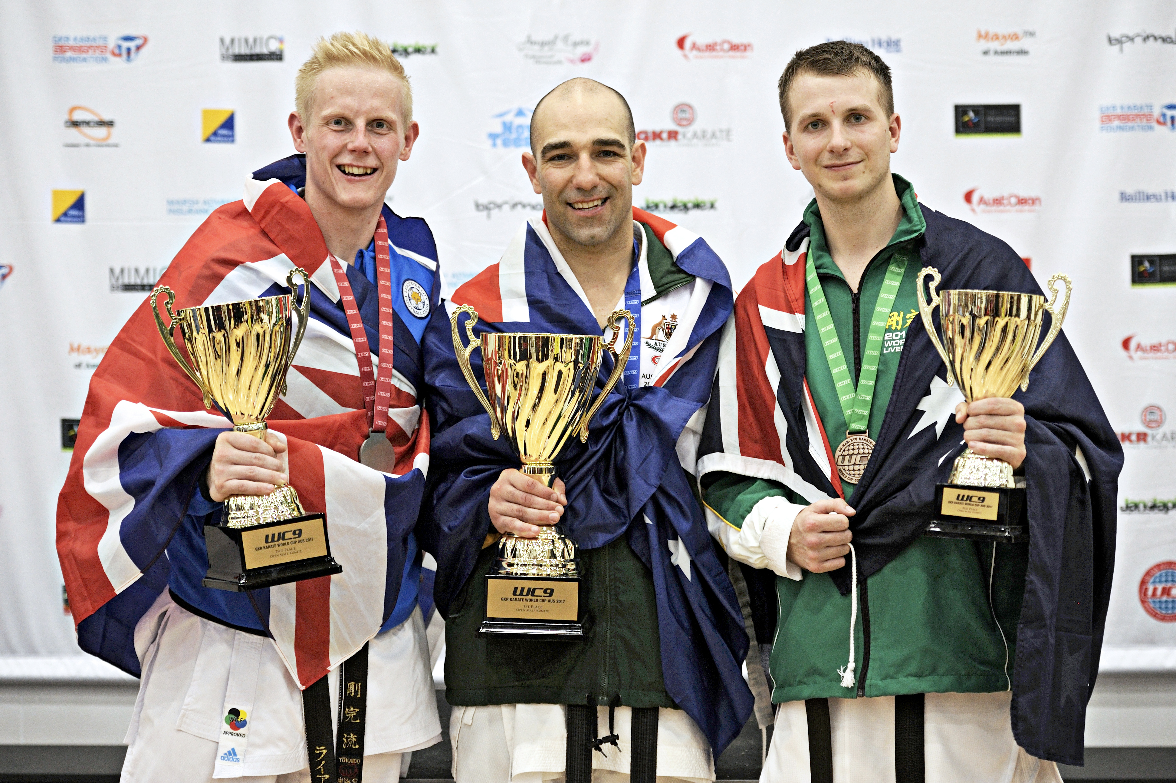 three men wearing there country flags, showing off their trophies