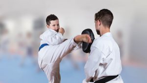 a young boy wearing a blue belt performs a karate kick move