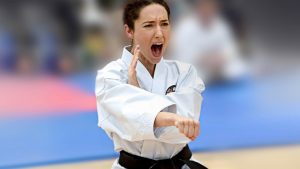 a young woman performs a karate stance, she wears a black belt