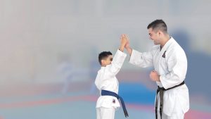 a young man wearing a black belt and a young boy wearing a blue belt give each other a high five
