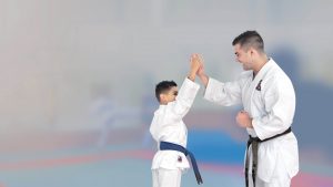 a young man wearing a black belt and a young boy wearing a blue belt give each other a high five