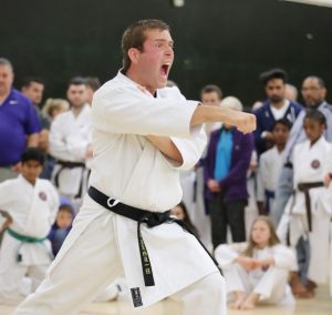 A young man performs a karate move in front of a crowd of onlookers