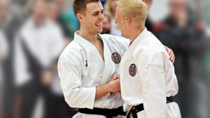 two young men wearing black belts give each other a handshake