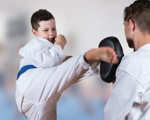 a young boy with a blue belt performs a kick towards a man holding a black pad