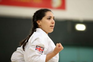 a young women wearing a gi that shows the united kingdom flag performs a karate move