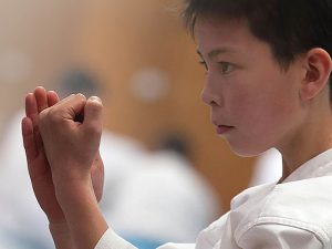 a young boy has his hands to his face performing a karate stance