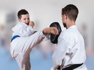 A young boy performs a kick to a boy who has protective gear