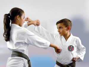 two small children with black belts, wearing karate gi's that have the gkr logo are performing karate moves
