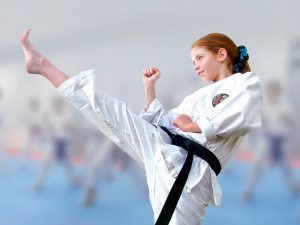 a small child with red hair, wearing a black belt and a gkr karate gi, performs a kick