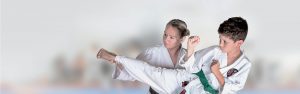 a young boy performs a karate move in front of a young girl who is also performing a karate move both young children wearing a gi