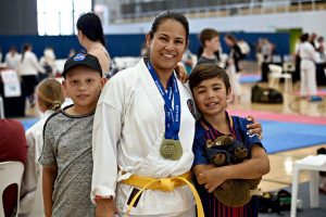 a family of three poses in front of the camera. Mother in the middle has two gold medals