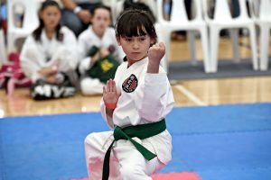 A little girl performs a karate move in front of an audience