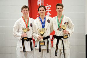 three teenage boys posing with medals and trophies