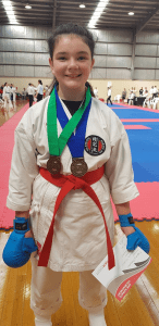 a young girl shows her two medals and certificate of participation