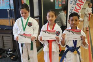 three young karate students showing off there gkr karate tournament certificate of participation