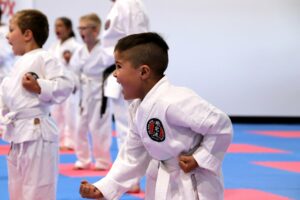a young child with other children in the background perform a karate stance, wearing a gkr karate gi and a white belt