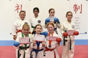 a group of young girls proudly showing off there karate certificates and belts