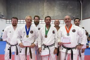 7 men stand in front of the camera with medals, and tickets of participation