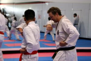 two men performing different karate stances, one has a red belt, the other has a black belt