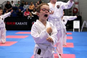 a small boy wearing glasses has a white belt, performing a karate stance