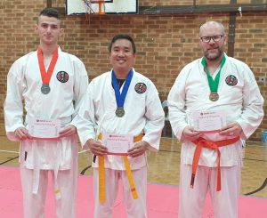 three middle aged men wearing gkr karate gi's, they have medals and certificate of participation