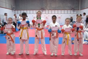 six kids standing proudly, wearing different coloured belts, showing there certificate of appreciation