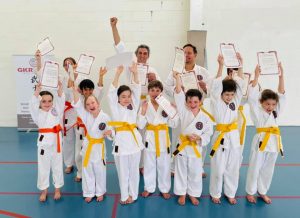 a group of students, some with orange belt, some with yellow, are cheering after they got there certificate of appreciation