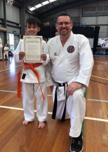 small boy wearing an orange belt stands tall next to a man wearing a white tip black belt