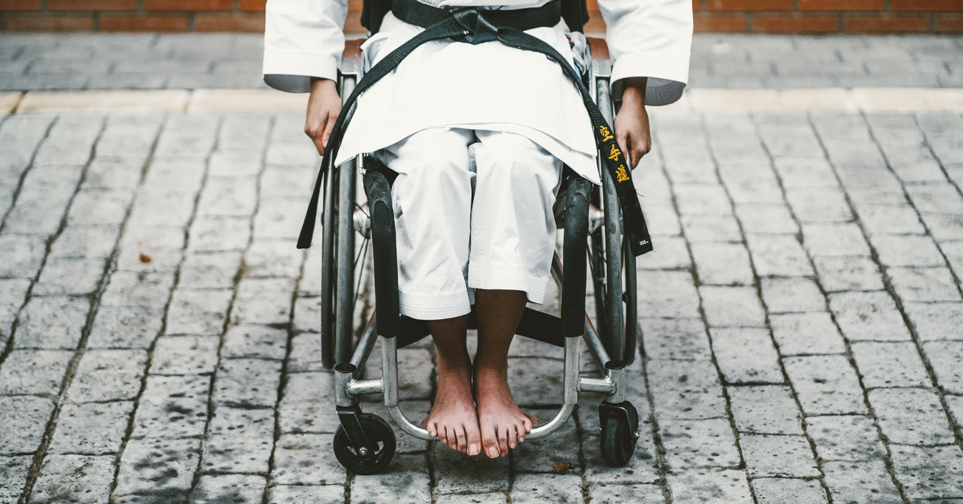 Woman in a wheelchair wearing a karate gi and black belt for the article Karate for people with disabilities