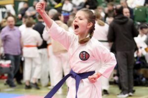 a little girl wearing a gkr karate gi, performing a karate move with a blue belt