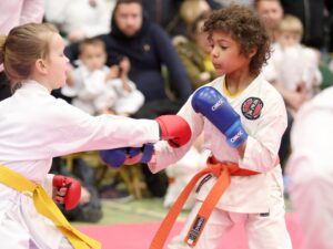 a little girl with a yellow belt punches a little boy wearing an orange belt