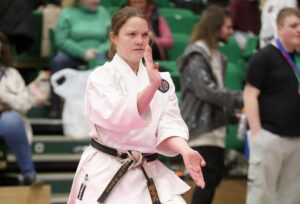 a woman wearing a gi performs a karate move, she is wearing a green belt